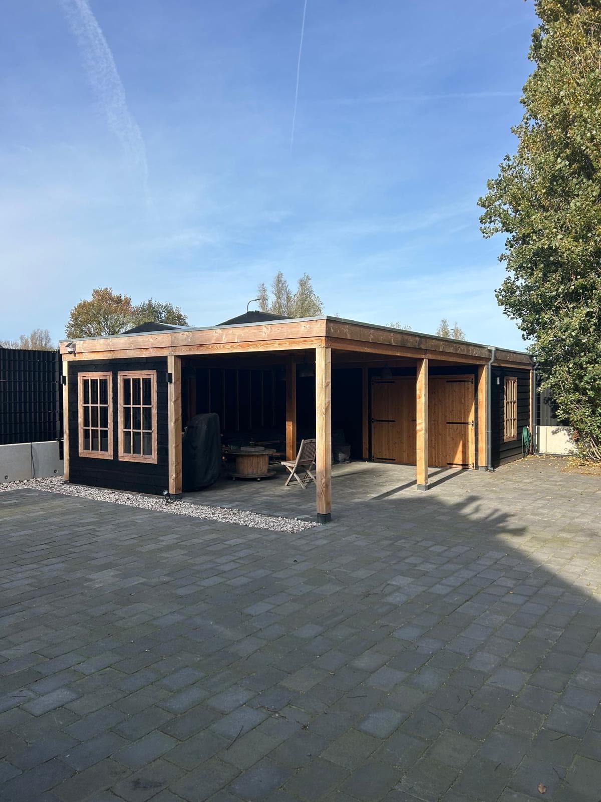 Black wooden garden house with canopy and clinker paving