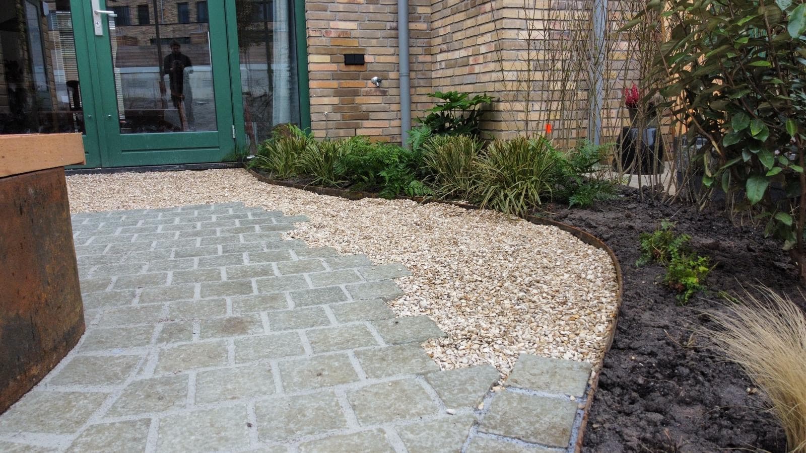 Natuurstenen bestrating overlopend in grind met cortenstalen kantopsluiting
