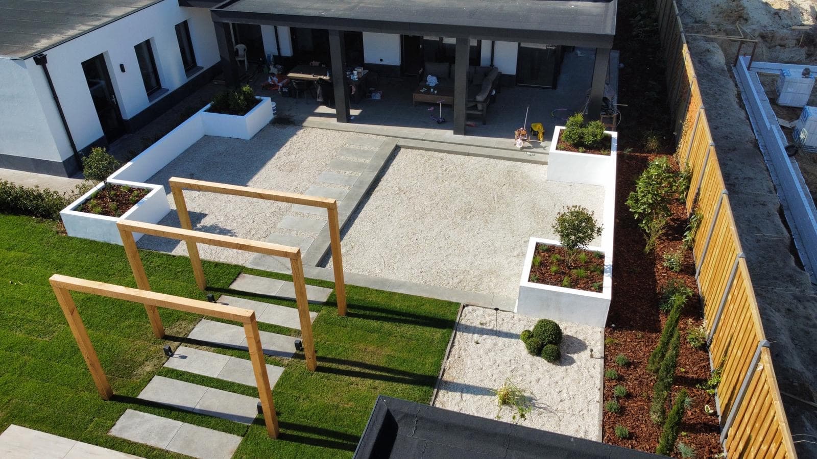 Strak tuinontwerp met witte plantenbakken, grind en houten portalen