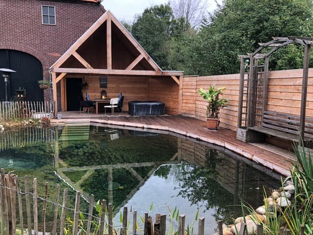 Natural swimming pond with clear water, wooden deck and oak veranda with hot tub